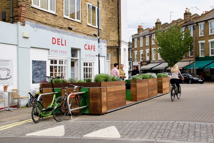 Modular parklet on a London street in front of a cafe deli, providing seating and bike parking