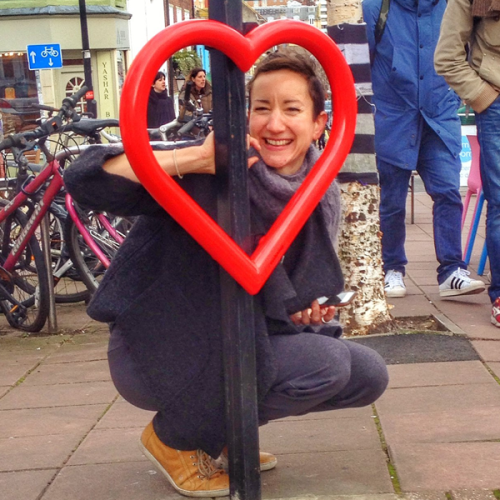 Person poses behind a Cyclehoop bike stand in the shape of a heart with a red finish