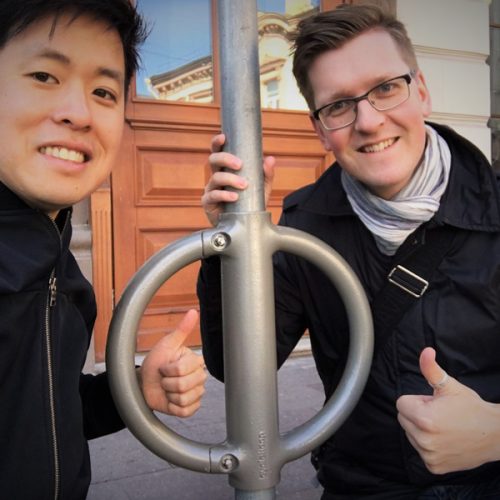 Two people stand next to a Cyclehoop bike stand on a city street