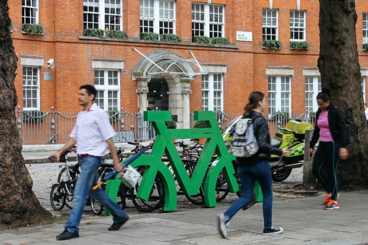 Busy street with a large green frame in the shape of a bike fixed to several bike stands to highlight bicycle parking