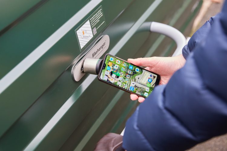 Cyclist using a smartphone to securely access a green Cyclehoop Bike Hangar