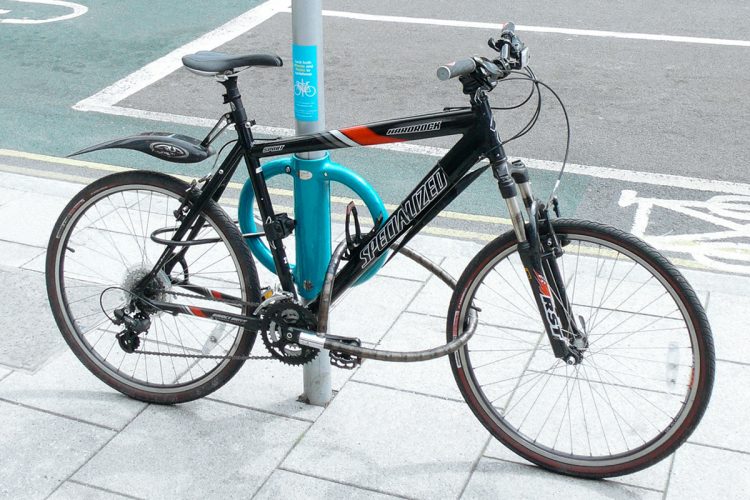 Black bike parked on blue Cyclehoop stand attached to street furniture