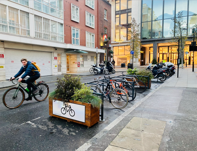 A side view of Cyclehoop Mobility Corral on a street with planters on either side and visible bike signage