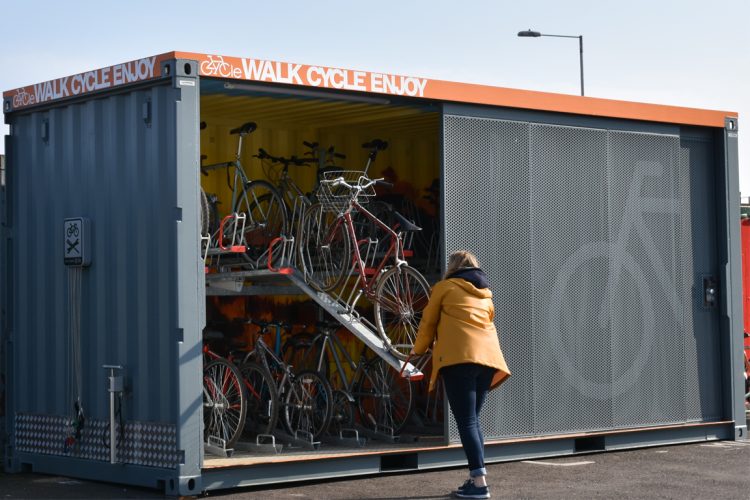 A cyclist with a yellow coat parks her bike on the top tier of the Cyclehoop Container Cycle Hub