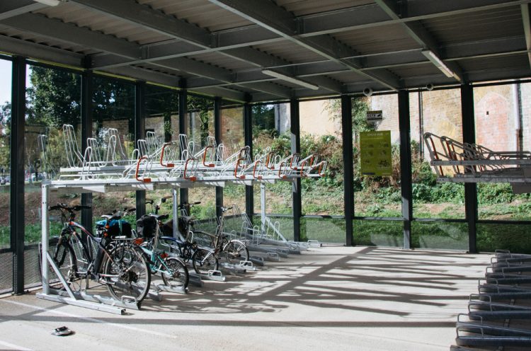 Inside of a Cycle Hub with glass walls, several parallel rows of empty two-tier bike racks, four bikes are parked on the bottom row
